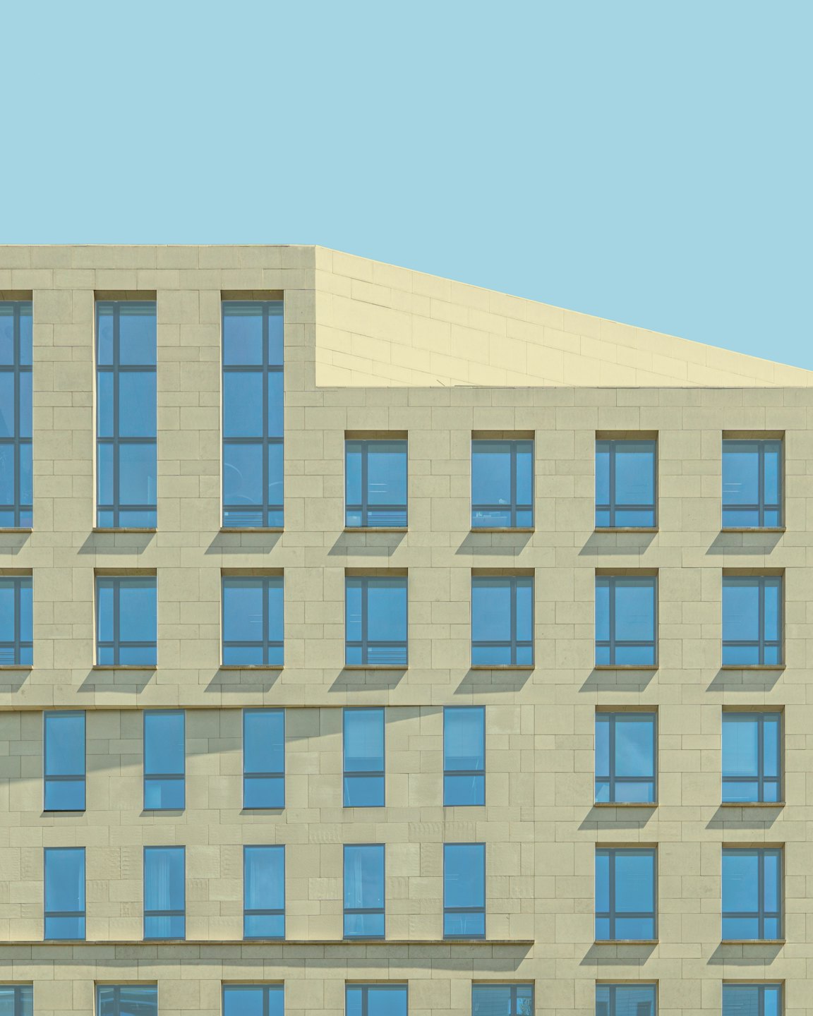 Moderne Gebäudefassade mit blau getönten Fenstern und Steinmauern.